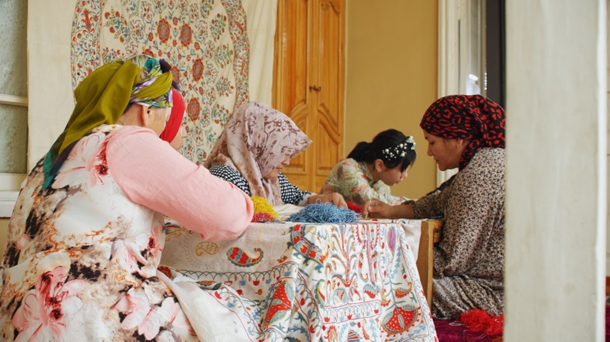 Fünf Frauen besticken einen Stoff mit traditionellen Mustern. 