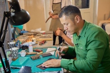 Kunsthandwerker von El-Nur Leather Craft sitzt an Werkbank und fertigt Lederprodukte.