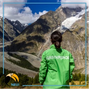 Eine Frau in einer grünen Jacke, auf der „Greenpeace“ steht vor einem Bergpanorama. 