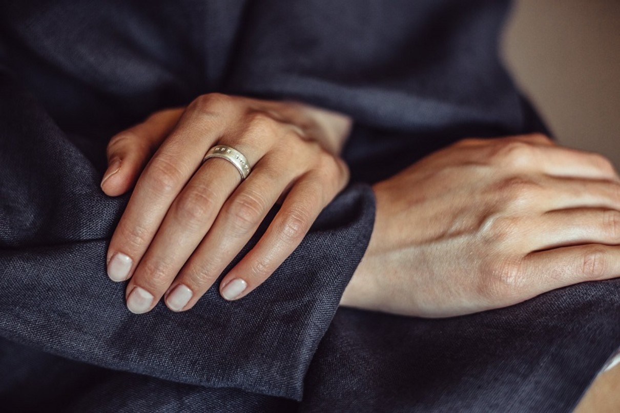 Zwei Hände, ein silberner Ring mit Aufschrift im Fokus.