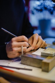 zwei Hände; ein Stift in der rechten Hand, etwas wird auf ein Material geschrieben. 